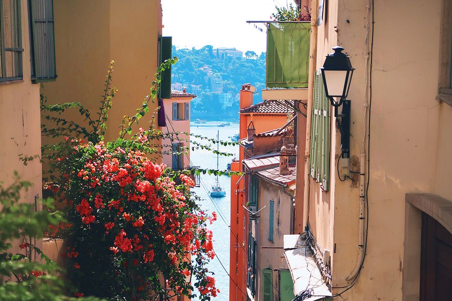 Eine enge, blumengeschmückte Straße führt zum Meer in Nizza, und fängt den Charme eines September-Urlaubs in Südfrankreich ein.