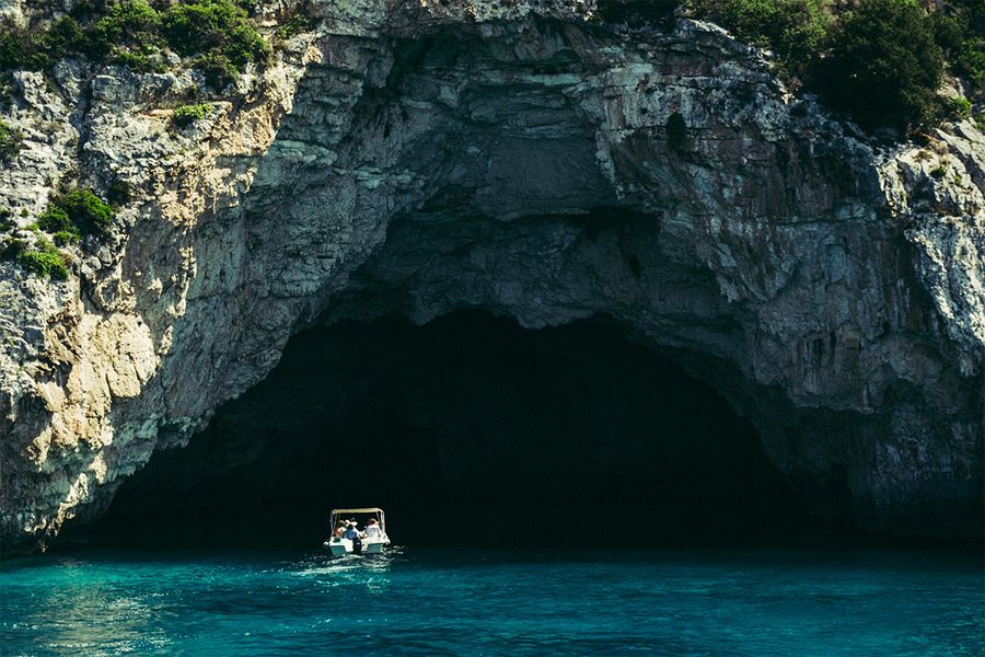 Ein Boot fährt in Meereshöhlen auf Korfu, und fängt das ruhige Tempo und die Schönheit eines griechischen Insel-Urlaubs im September ein.