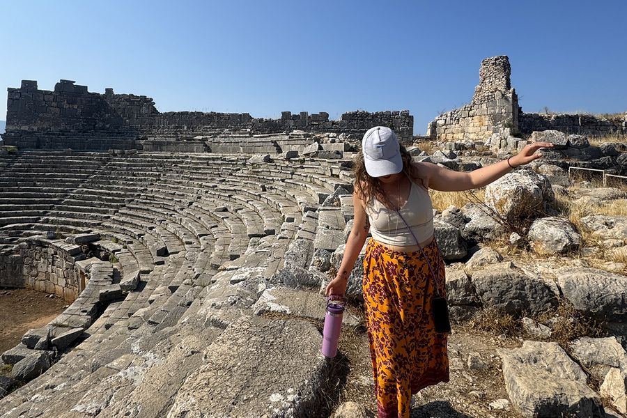 Gemma, Texterin bei posterXXL, geht zwischen den Felsen eines Amphitheaters in Kalkan, Türkei, und veranschaulicht, wie man das richtige September-Reiseziel für den Urlaub wählt.