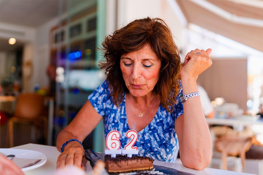 Eine Frau pustet die Kerzen aus, die die Zahl '62' auf ihrer Geburtstagstorte zeigen, und veranschaulicht posterXXLs Tipp, den genauen Moment festzuhalten, in dem die Kerzen ausgeblasen werden.