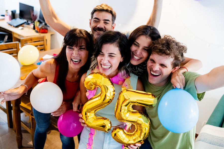 Eine Gruppe junger Leute versammelt sich um Ballons mit der Zahl '25', lächelt und posiert für ein Foto, und veranschaulicht posterXXLs Tipps zum Festhalten besonderer Geburtstagsmomente.