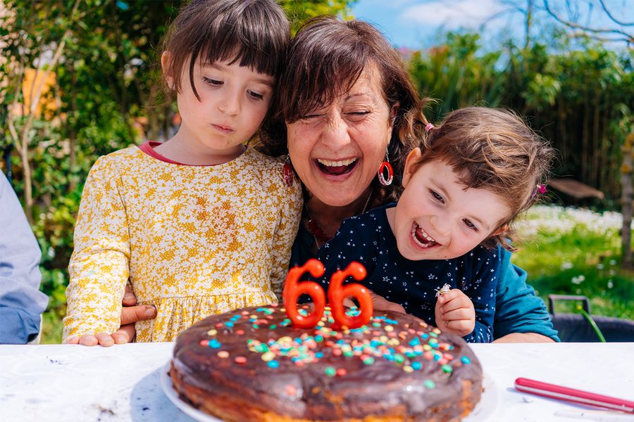 Eine Frau lächelt neben ihrer Geburtstagstorte mit Kerzen, die '66' zeigen, flankiert von zwei lächelnden Kindern, und veranschaulicht posterXXLs Tipps zum Festhalten generationsübergreifender Geburtstagsmomente.