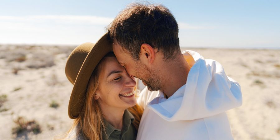 Ein Paar Anfang dreißig lächelt und umarmt sich in einer strandähnlichen, wüstenartigen Umgebung, und stellt posterXXLs Ratgeber mit 60 Ideen für Nachrichten in einer Hochzeitstagskarte vor.