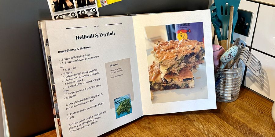 Ein aufgeschlagenes persönliches Kochbuch liegt in einer Küche, mit einem Glas voller Löffel und Küchenutensilien im Hintergrund, und stellt posterXXLs Ratgeber zum eigenen Kochbuch erstellen vor.