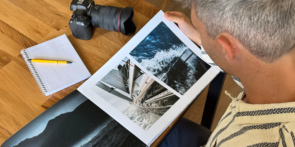 Fotograf Charl van Rooy schaut auf sein Portfolio, mit seiner Kamera und einem Notizbuch auf dem Tisch neben sich, und stellt posterXXLs Ratgeber zum Erstellen eines Fotografie-Portfolios als Fotobuch vor.