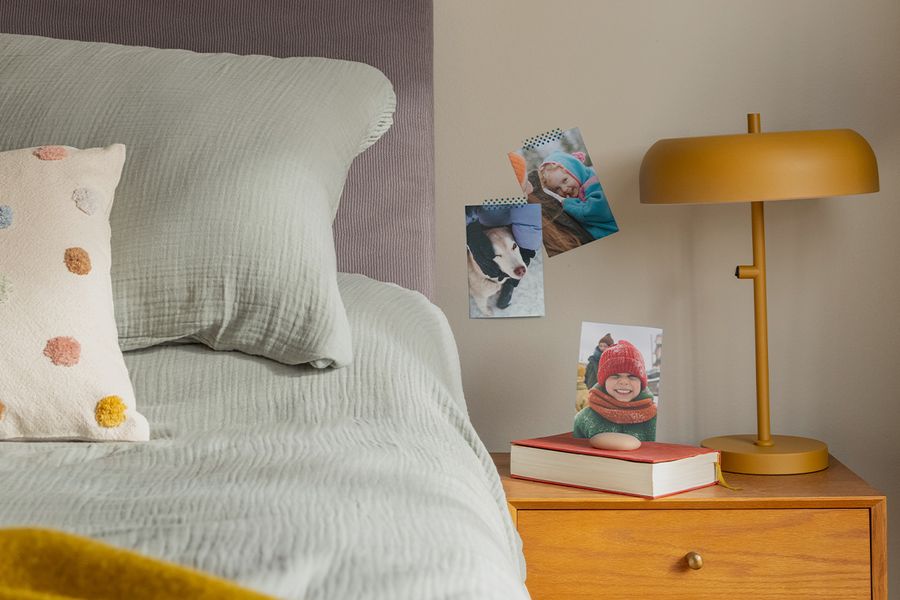 Eine Auswahl an Familienfotoabzügen hängt an der Wand neben einem Bett, und veranschaulicht, wie posterXXLs Fotoabzüge einem Hygge-Schlafzimmer eine gemütliche, persönliche Note verleihen.