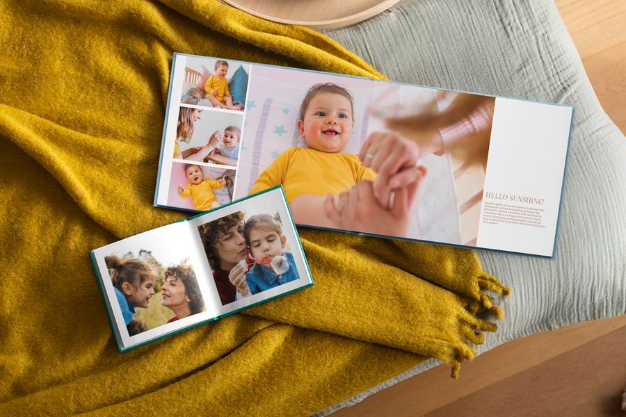 Zwei aufgeschlagene personalisierte Fotobücher mit Familienbildern liegen auf einer senfgelben Decke und veranschaulichen, wie posterXXLs Fotobücher in ein Hygge-Zuhause passen.