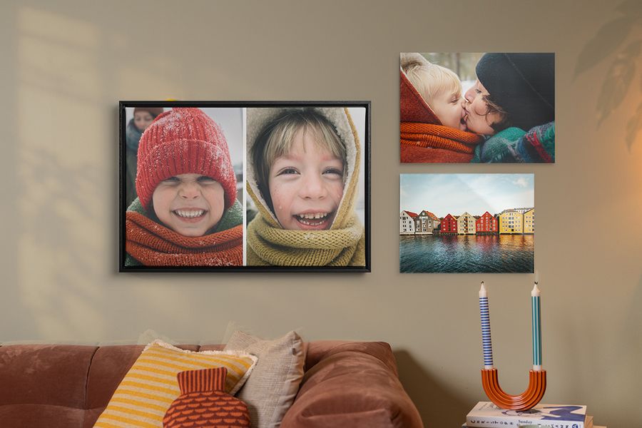 Drei Beispiele für personalisierte Wandkunst hängen über einem Sofa in einem Wohnzimmer, herbstliche Familienbilder mit lächelnden Kindern in Winterkleidung, und veranschaulichen, wie posterXXLs Wandkunst dem Zuhause einen gemütlichen Hygge-Stil verleiht.