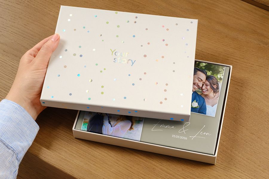 Ein Hochzeitsfotobuch liegt in der neuen Präsentationsbox, mit einem Bild des Paares und dem Hochzeitsdatum als Titel auf dem Cover, teilweise verdeckt durch den leicht geöffneten Deckel der Geschenkbox, und veranschaulicht, warum sich eine Präsentationsbox für ein hochwertiges Hochzeitsfotobuch lohnt.