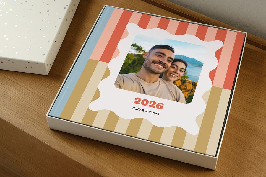 Ein Fotobuch liegt ohne Deckel in der Geschenkbox und wirkt wie ein Jahrbuch mit der Aufschrift '2026' und einem lächelnden Paar auf dem Cover, und veranschaulicht, wie man die richtige Größe der Präsentationsbox für sein Fotobuch auswählt.