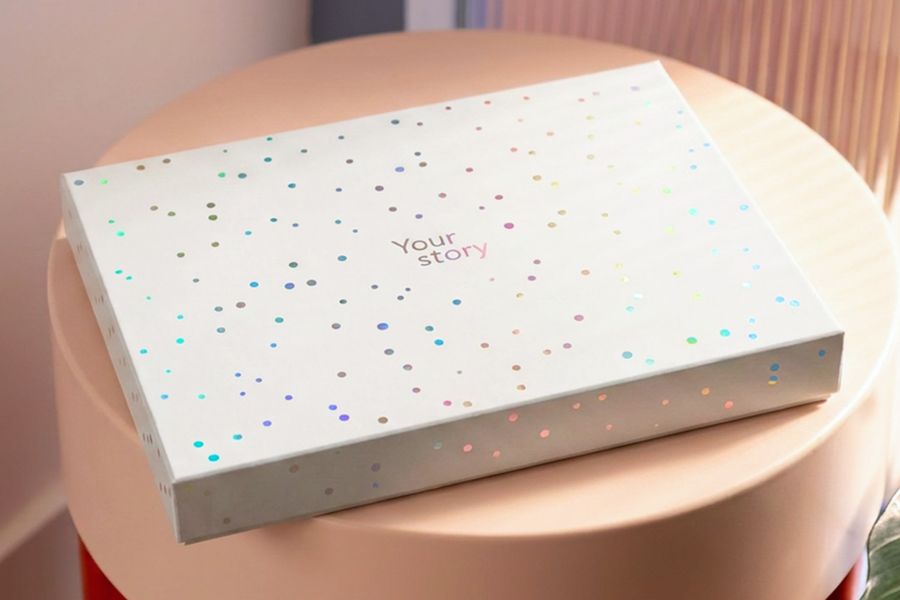 Die geschlossene Präsentationsbox steht auf einem Hocker, und zeigt das fertige Erscheinungsbild von posterXXLs neuer Fotobuch-Geschenkbox.