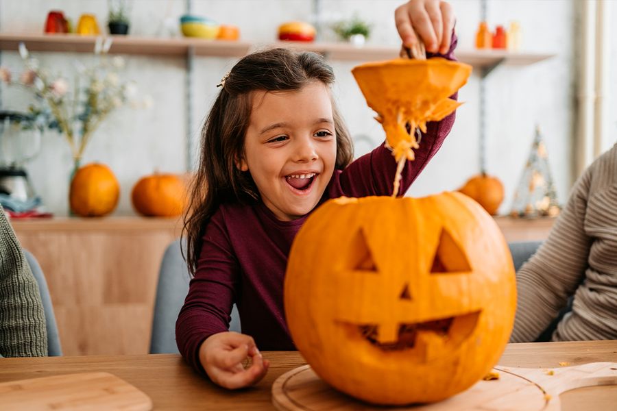 Ein Kind hebt den Deckel eines Kürbisses ab, den es gerade geschnitzt hat, und veranschaulicht posterXXLs lustige und süße Kürbis-Sprüche für Halloween-Bildunterschriften auf Instagram.