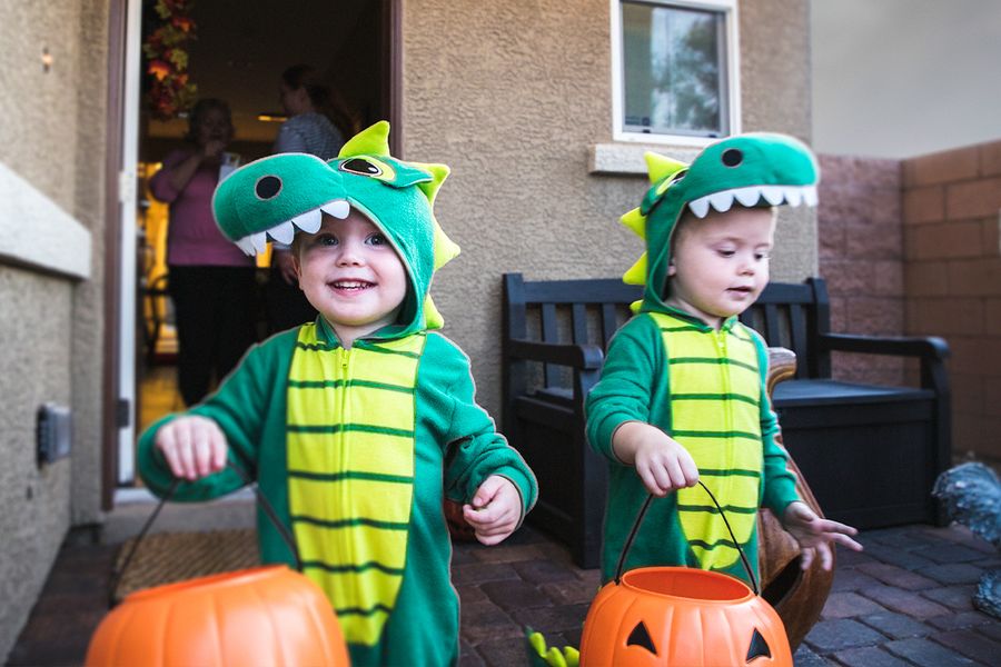 Zwei kleine Jungen in Dinosaurier-Kostümen gehen von Haus zu Haus und halten Kürbis-Körbchen in den Händen, und veranschaulichen posterXXLs Halloween-Sprüche für Fotos vom Süßes-oder-Saures-Gehen.