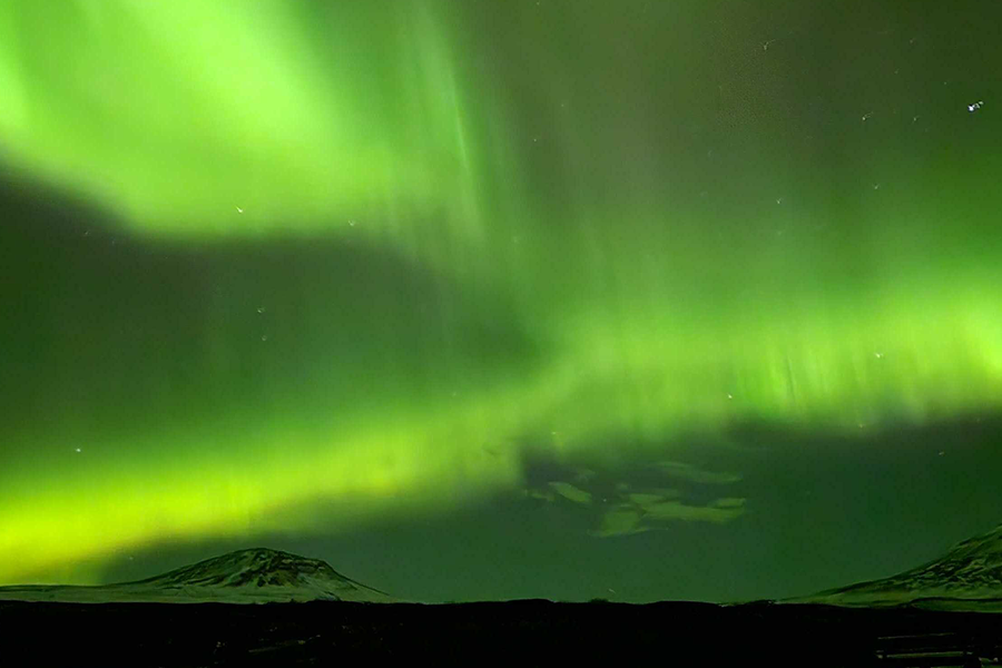 Schneebedeckte Berge unter einem durch die Polarlichter sehr grün gefärbten Himmel, zur Illustration von posterXXLs Tipps, wo man Polarlichter sehen kann, ohne nach Island zu reisen.