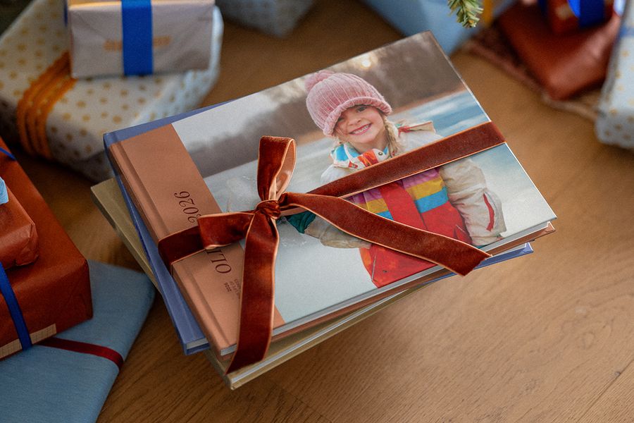 Stapel personalisierter Fotobücher, um die ein braunes Samtband gebunden ist, mit weiteren verpackten Geschenken im Hintergrund, passend zu posterXXLs Tipps zum Planen von Weihnachtsgeschenken mit persönlichen Fotos.