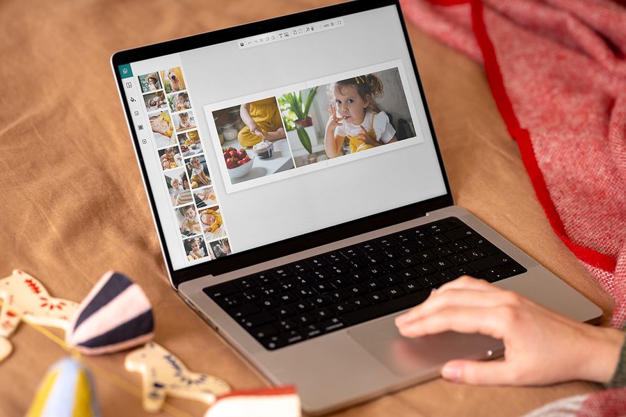 Eine Hand auf dem Touchpad eines Laptops gestaltet ein Fotobuch auf dem Bildschirm mit einer Doppelseite, die ein kleines Mädchen und eine Schale Erdbeeren zeigt, als Illustration für posterXXLs Online-Editor für Black-Friday-Weihnachtsgeschenke.