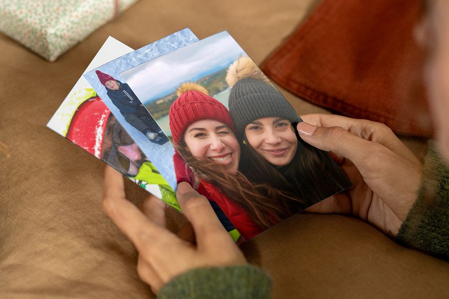 Person, die Fotoabzüge in den Händen hält, wobei der vorderste zwei lächelnde Frauen in Wintermützen und Wintermänteln zeigt, passend zu posterXXLs Tipps, um die richtigen Fotos für ein personalisiertes Fotogeschenk zu finden.