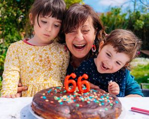 Oma bläst mit ihren beiden Enkeln glücklich Geburtstagskerzen aus.