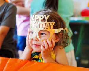 Ein kleines Mädchen trägt eine goldene "Happy Birthday"-Maske.