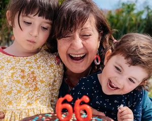 Eine Großmutter feiert ihren 66. Geburtstag mit ihren beiden Enkelkindern an ihrer Seite und möchte gerade die Kerzen auf ihrer Torte ausblasen – als Inspiration für Geburtstagsgeschenke aus dem ultimativen Geburtstagsgeschenke-Guide von posterXXL.