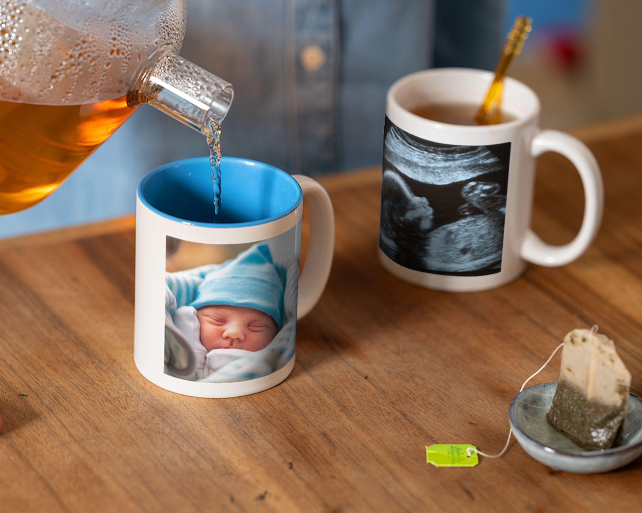 Tee, der in eine personalisierte Tasse mit einem Baby-Foto eingeschenkt wird, neben einer Tasse mit Ultraschallfoto.