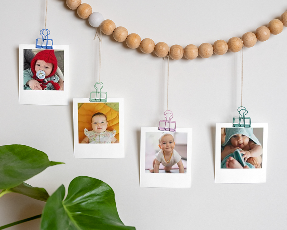 Babyfotos an einer aus Holz gefertigten Perlengirlande, die an der Wand hängt.