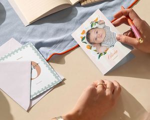 Hände, die eine personalisierte Babyfotokarte am Schreibtisch schreiben.