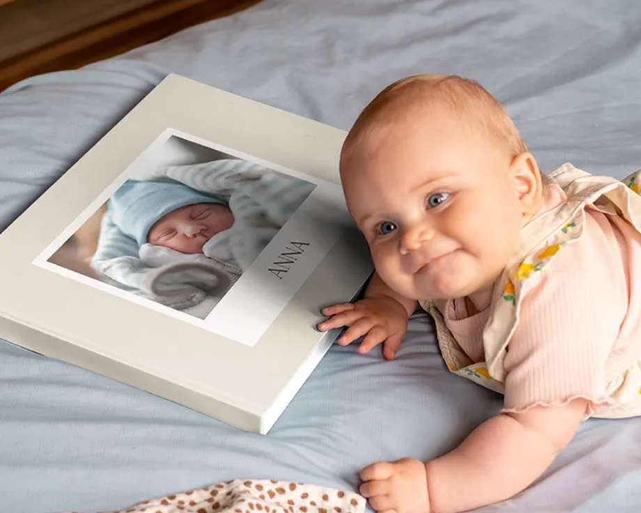 Baby liegt neben einem personalisierten Fotobuch mit einem Babybild auf dem Cover.
